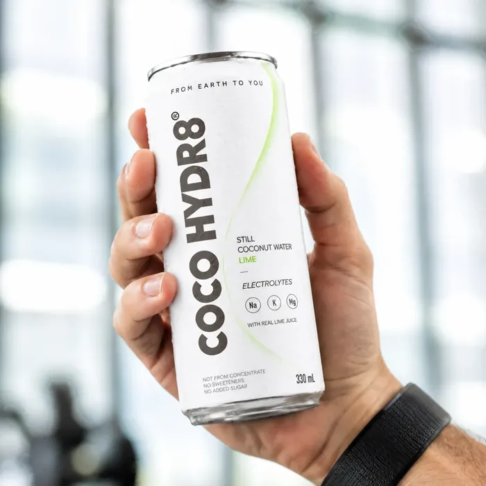 A hand holding a can of COCO HYDR8 Lime up in a bright gym