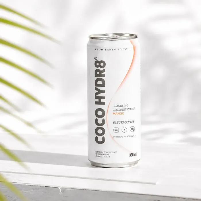 A can of COCO HYDR8 Mango on a white wooden ledge in the shade of a palm leaf