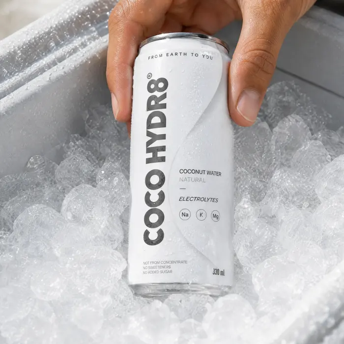 A hand lifting a can of COCO HYDR8 Natural out of a cooler full of ice