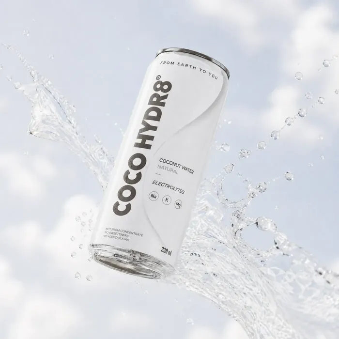 A can of COCO HYDR8 Natural in a sweeping splash of water against a pale sky