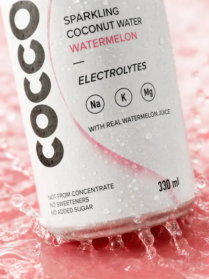 The base of a can of COCO HYDR8 Watermelon landing in pink water, droplets flying